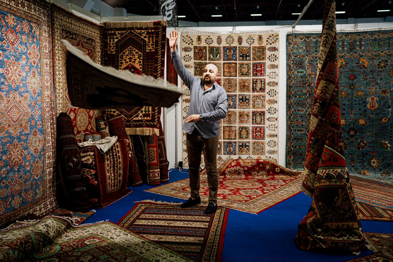about-02 A man showcases traditional Persian rugs at an indoor market stall.